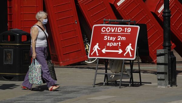 Женщина в медицинской маске и плакат с призывом соблюдать социальную дистанцию на фоне скульптуры британского скульптора Дэвида Маха Out of Order в Лондоне, Великобритания  - Sputnik Литва