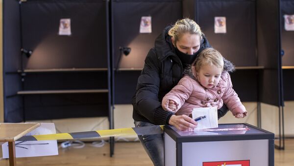 Женщина с ребенком опускает свой бюллетень на избирательном участке во время второго тура парламентских выборов в Вильнюсе, 25 октября 2020 года - Sputnik Литва