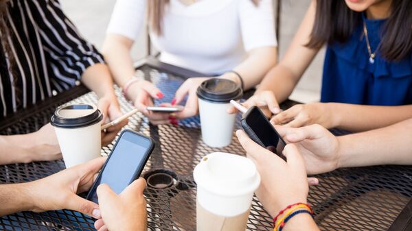 Молодые люди сидят в кафе с мобильными телефонами - Sputnik Lietuva
