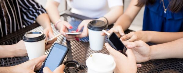 Молодые люди сидят в кафе с мобильными телефонами - Sputnik Литва