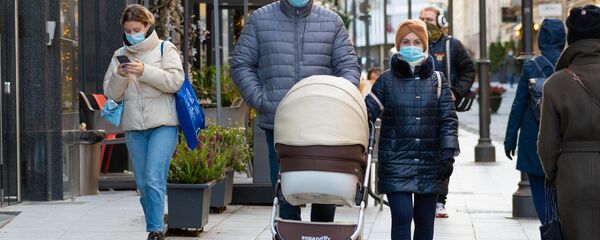 Пара в защитных масках с коляской, гуляют по улице в Вильнюсе - Sputnik Литва