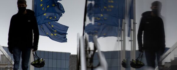 Мужчина идет мимо флагов ЕС у штаб-квартиры ЕС в Брюсселе - Sputnik Литва