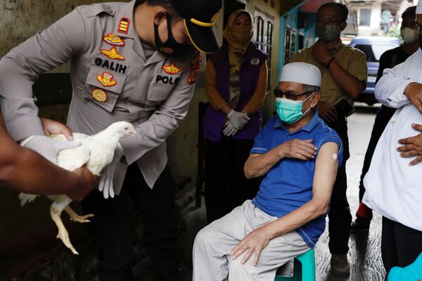Rajono policijos viršininkas Galihas Apria duoda gyvą vištą 68 metų Sindanglajos kaimo gyventojui Jeje Jaenudin, kuris ką tik gavo pirmąją COVID-19 vakcinos dozę, vakcinacijos metu Siandžuro regione, Vakarų Javos provincijoje, Indonezijoje, 2021 metų birželio 15 diena. - Sputnik Lietuva