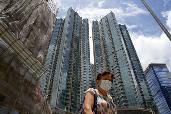 Moteris, užsidėjusi veido kaukę, kuri padeda išvengti koronaviruso plitimo, eina priešais Grand Central gyvenamųjų pastatų kompleksą Honkonge, 2021 metų birželio 15 dieną, antradienį. Nekilnojamojo turto agentai pasiūlė 10,8 mln. HK (1,4 mln. USD) 449 kvadratinių metrų ploto vieno kambario butą kaip prizą pagal laimingąjį burtą, siekiant padidinti Honkongo COVID-19 vakcinacijos rodiklius. - Sputnik Lietuva