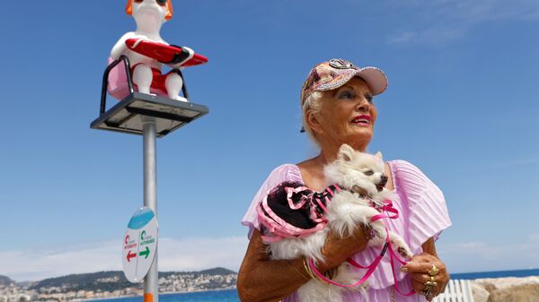 Moteris Nicoje, Prancūzijoje, Promenade des Anglais alėjoje, laiko savo šunį ant rankų šunų paplūdimyje. - Sputnik Lietuva