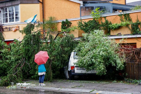 Moteris stovi priešais mikroautobusą, kurį per perkūniją ir stiprų lietų apgadino nukritęs medis Ciuriche, Šveicarijoje. - Sputnik Lietuva