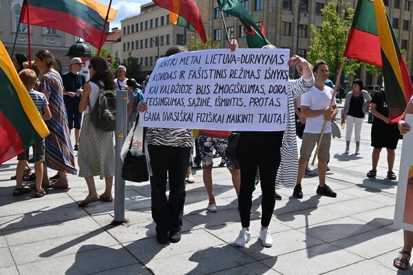Protesto dalyvės su plakatu &quot;Antri metai Lietuva = durnynas. Kovidas ir fašistinis režimas išnyks, kai valdžioje bus žmogiškumas, dora, teisingumas, sąžinė, išmintis, protas. Gana dvasiškai, fiziškai naikinti tautą&quot;. - Sputnik Lietuva