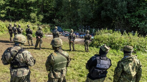 Польские пограничники стоят рядом с группой мигрантов на границе Польши и Белоруссии - Sputnik Литва