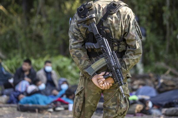 Вооруженный польский пограничник перед группой мигрантов в лагере на границе Белоруссии и Польши. - Sputnik Литва