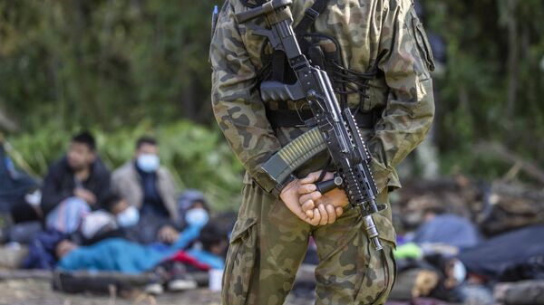 Вооруженный польский пограничник перед группой мигрантов в импровизированном лагере на границе Белоруссии и Польши - Sputnik Литва