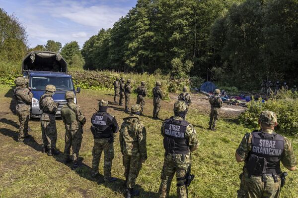 Польские и белорусские пограничники стоят рядом с группой мигрантов на границе Польши и Белоруссии. - Sputnik Литва