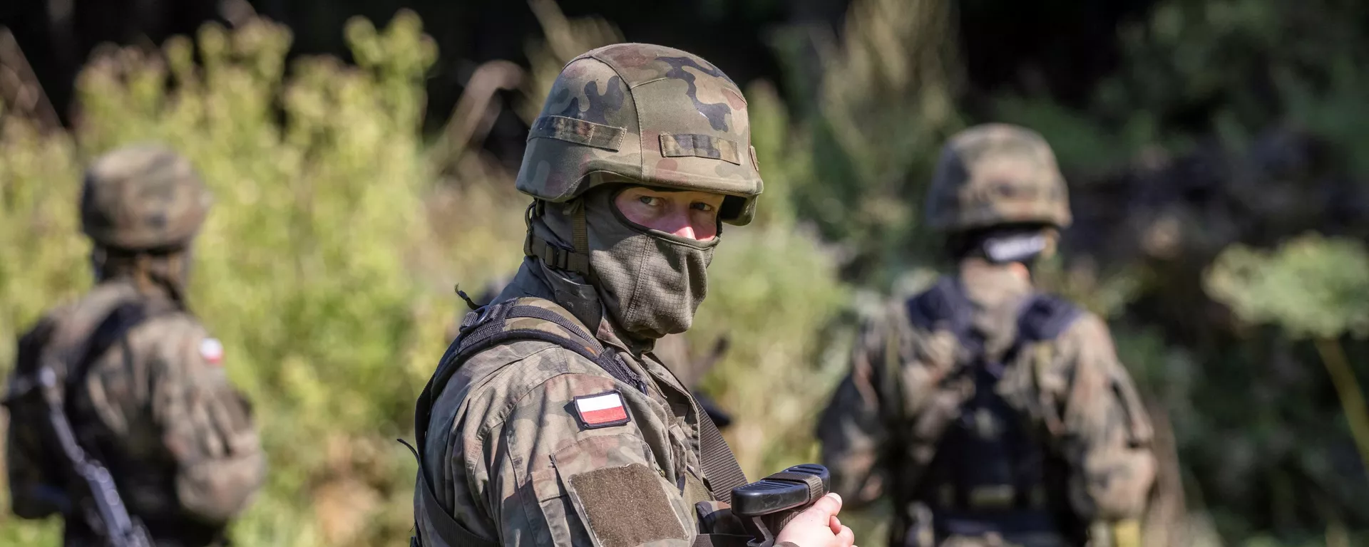 Вооруженный польский пограничник рядом с группой мигрантов в импровизированном лагере на границе между Беларусью и Польшей - Sputnik Lietuva, 1920, 22.09.2021