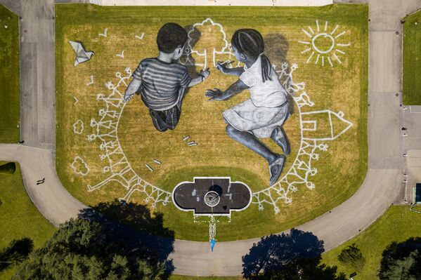 Šioje nuotraukoje, padarytoje Jungtinių Tautų biuro parke Ženevoje, matomas Saype paveikslas, kurį užsakė Šveicarija, minint 75-ąsias Jungtinių Tautų Chartijos pasirašymo metines. 6 tūkst. kvadratinių metrų piešinys, pavadintas &quot;World in Progress&quot;, vaizduoja du vaikus, piešiančius savo idealų pasaulį. - Sputnik Lietuva
