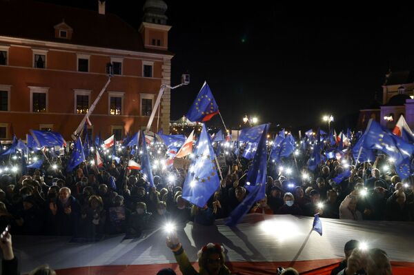Dalyviai per mitingą laiko savo mobiliuosius telefonus su šviesomis ir mosuoja ES vėliavomis virš didelės Lenkijos vėliavos. - Sputnik Lietuva