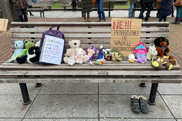 Protestuotojai ant suoliukų prie Vyriausybės pastato paliko minkštus žaislus. Plakatas dešinėje skelbia: &quot;NE!!! Priverstinei ir vaikų vakcinacijai!&quot; - Sputnik Lietuva