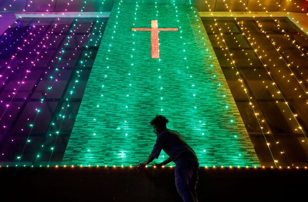 Vyras prieš šventes kabina dekoratyvines lemputes prie bažnyčios, Indijoje. - Sputnik Lietuva
