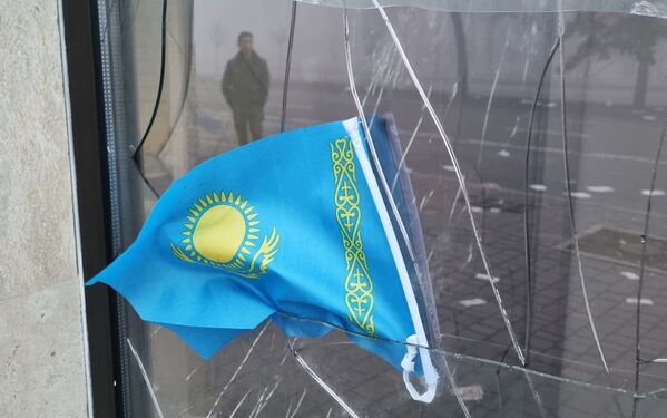 Kazachstano valstybės vėliava matoma prie išdaužto Kaspi banko filialo lango po protestų, kuriuos sukėlė kuro kainų kilimas Almatoje, Kazachstane 2022 metų sausio 6 dieną. - Sputnik Lietuva