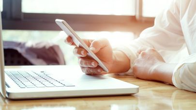 Мужчина за ноутбуком со смартфоном в руках, архивное фото