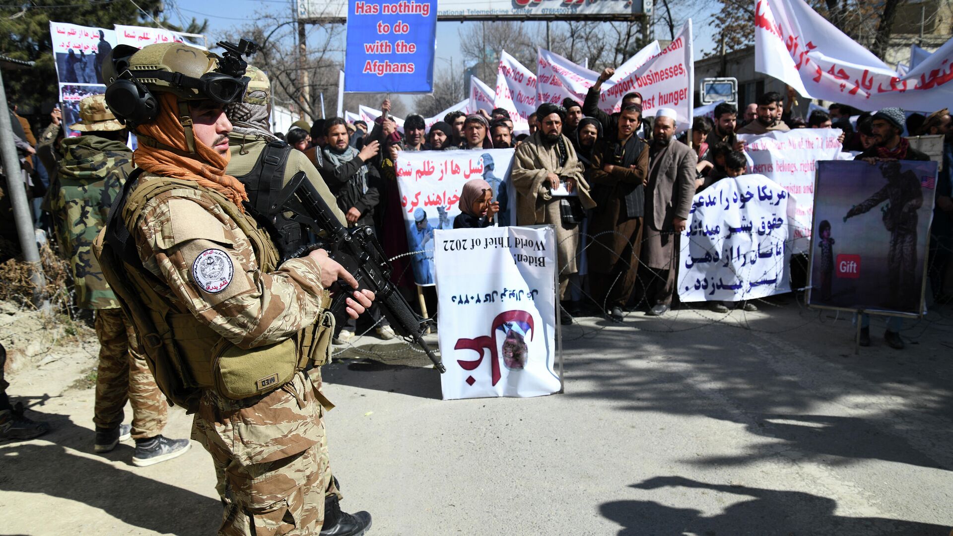 Talibano kovotojas ir žmonės su plakatais per protesto eitynes ​​prieš JAV prezidento Džo Baideno pareiškimus Kabule - Sputnik Lietuva, 1920, 18.02.2022