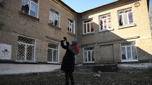 Женщина осматривает поврежденные в результате обстрела окна в здании школы в Донецке - Sputnik Литва