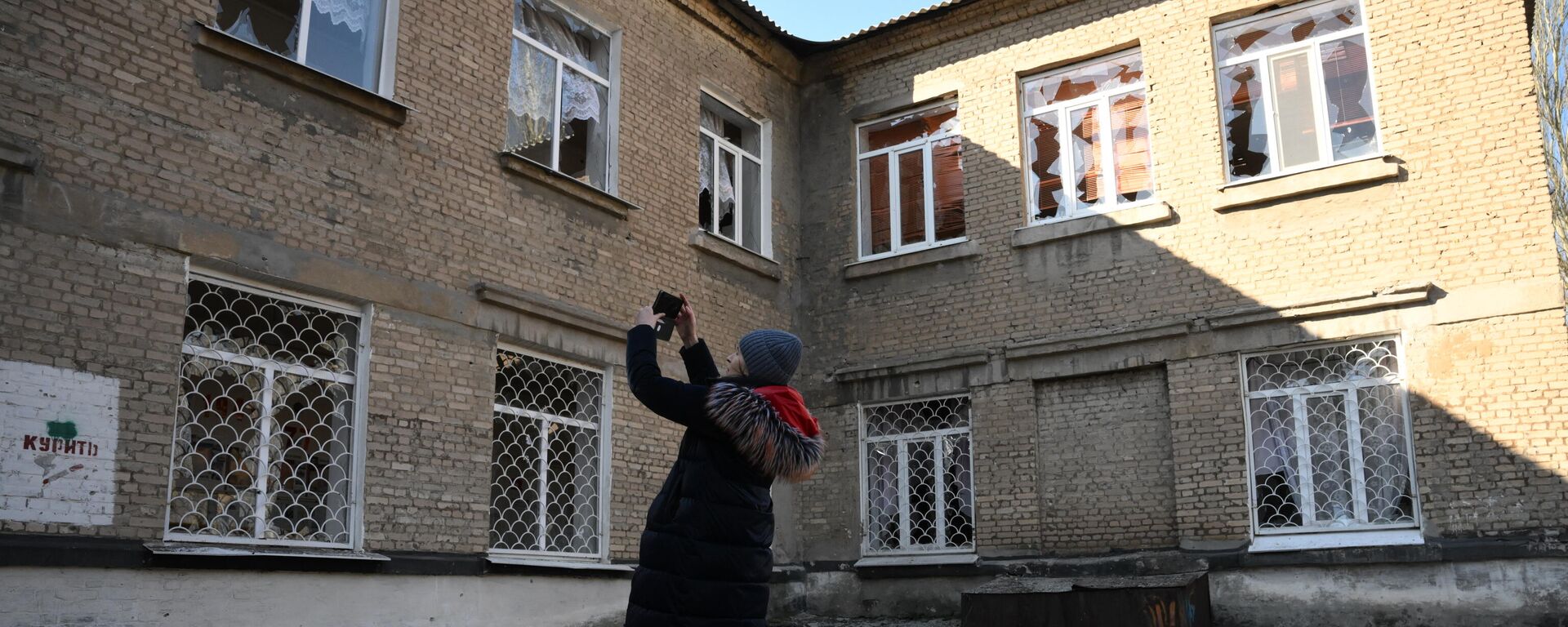 Женщина осматривает поврежденные в результате обстрела окна в здании школы в Донецке - Sputnik Литва, 1920, 23.02.2022