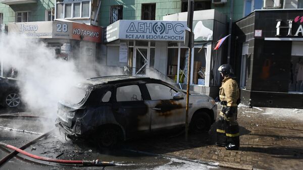 Сотрудник пожарной охраны у сгоревшей машины в центре Донецка - Sputnik Литва