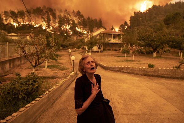 Graikijos fotografo Konstantino Tsakalidiso, laimėtojo kategorijoje &quot;EUROPE SINGLES&quot;, nuotrauka &quot;Evia Island Wildfire&quot;. 81 metų Kritsiopi Panayiota rugpjūčio 8 d. reaguoja į gaisrą, artėjantį link jos namo Gouves kaime, Evijos saloje, Graikijoje. Po ilgo karščio laikotarpio Graikijoje buvo karščiausias oras per 30 metų, tūkstančiai gyventojų evakuota valtimi dėl gaisrų, prarijusių antrąją pagal dydį Graikijos salą. - Sputnik Lietuva