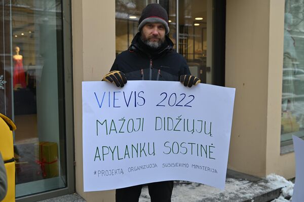 На фото: участник акции протеста держит плакат с надписью &quot;Вевис-2022 — маленькая столица больших объездов&quot;. - Sputnik Литва