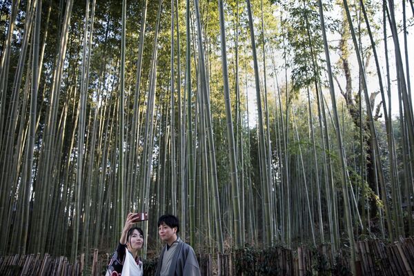 На фото: туристы делают селфи в бамбуковом лесу Сагано, который находится в Киото, Япония.История парка восходит к XIV веку, когда японский монах, поэт и мастер садового искусства Мусо Сосэки решил создать живописный парк с видом на горы и храмовые комплексы. Сегодня это популярное туристическое место. Кстати, здесь можно услышать мелодичные звуки, которые напоминают популярные на Востоке ветряные колокольчики, — их издают бамбуковые стебли, качаясь от дуновения ветра. - Sputnik Литва