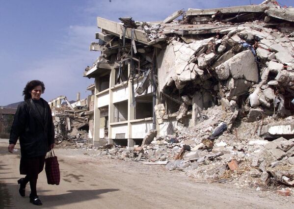 На фото: женщина идет мимо разрушенного после бомбардировок НАТО здания в Косовска-Митровице, Югославия. - Sputnik Литва