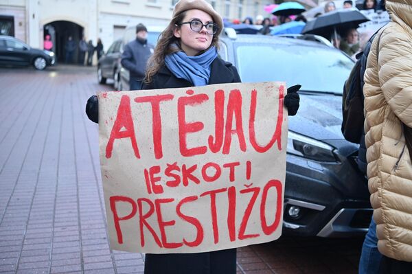 На фото: участница акции протеста держит плакат с надписью: &quot;Пришла искать престиж&quot;. - Sputnik Литва