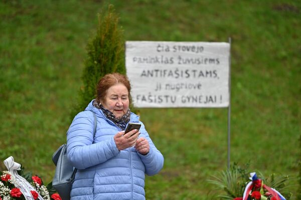 На фото: женщина стоит возле таблички рядом со снесенным мемориалом, на которой написано: "Здесь стоял памятник погибшим антифашистам, его снесли пособники фашистов". - Sputnik Литва