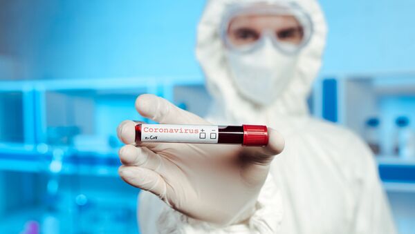 Сотрудник лаборатории в защитном костюме держит образец крови с коронавирусом - Sputnik Литва