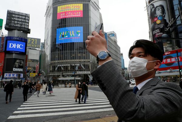 Мужчина в защитной маске фотографирует на мобильный телефон в полдень на перекрестке Сибуя в Токио во время пандемии коронавируса  - Sputnik Литва