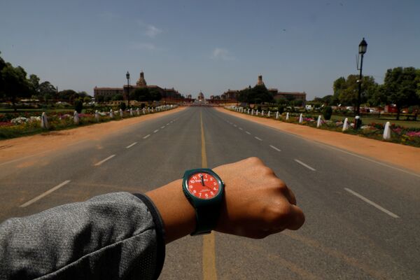 Показывающие полдень наручные часы на фоне пустого проспекта Раджпатх в Нью-Дели в период пандемии коронавируса - Sputnik Литва