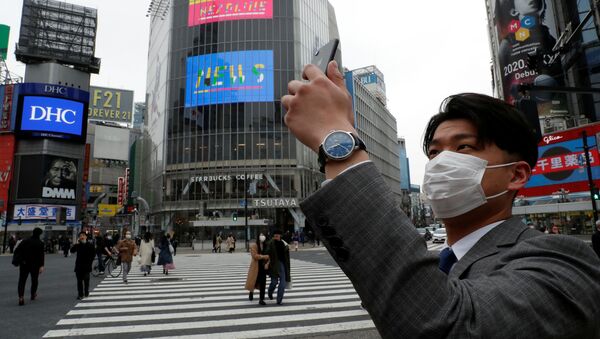 Мужчина в защитной маске фотографирует на мобильный телефон в полдень на перекрестке Сибуя в Токио во время пандемии коронавируса  - Sputnik Lietuva