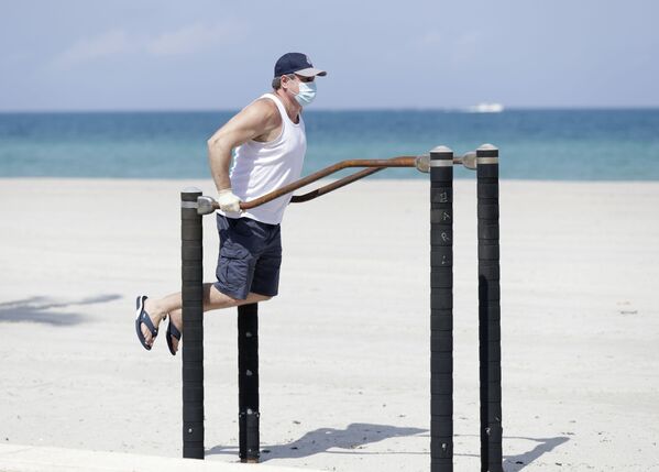 Мужчина в защитной маске во время выполнения упражнений на турнике на пляже в Голливуде, США - Sputnik Lietuva