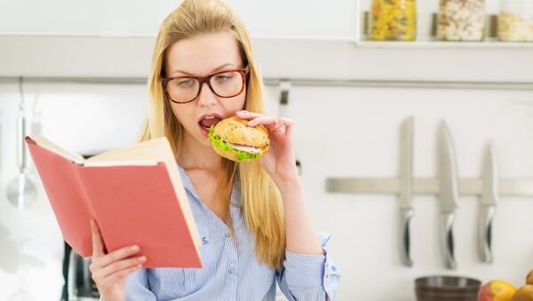 Девушка ест гамбургер во время чтения - Sputnik Литва