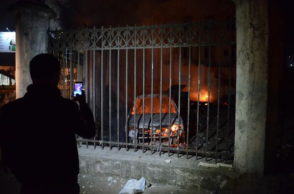 Человек фотографирует на смартфон сожженные в ходе беспорядков в Батуми машины - Sputnik Литва