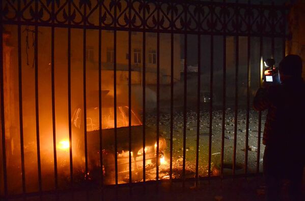 Оператор одного из грузинских телеканалов снимает сожженную в ходе беспорядков в Батуми машину - Sputnik Литва