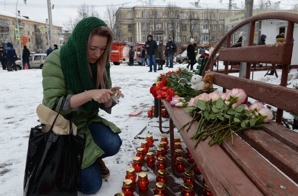 Женщина зажигает свечу возле здания торгового центра Зимняя вишня в Кемерово, где произошел пожар - Sputnik Lietuva