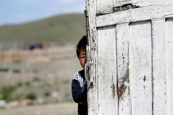 Пятилетний сын жителя монгольской деревни выглядывает из-за ворот на окраине Улан-Батора - Sputnik Lietuva