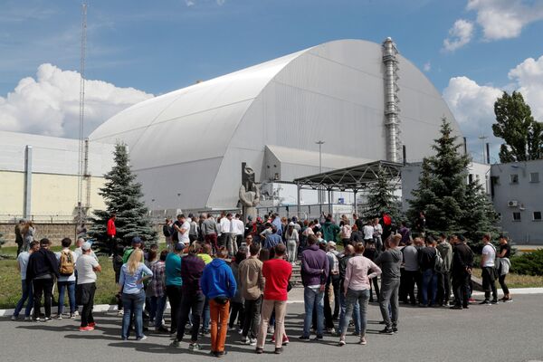 Посетители стоят возле здания Нового безопасного конфайнмента (НБК) над старым саркофагом, покрывающим поврежденный четвертый реактор на Чернобыльской АЭС, в Чернобыле, Украина, 2 июня 2019 года - Sputnik Lietuva