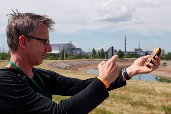 Посетитель фотографирует дозиметр возле структуры «Новый безопасный конфайнмент» (НБК) над старым саркофагом, покрывающим поврежденный четвертый реактор на Чернобыльской АЭС, в Чернобыле, Украина, 2 июня 2019 года - Sputnik Lietuva